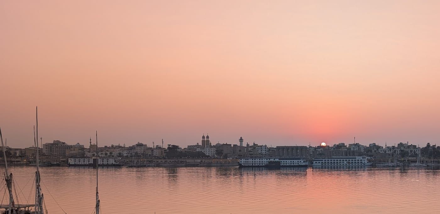 Sunrise over Luxor's East Bank across the Nile, with the city skyline beneath an orange sky.