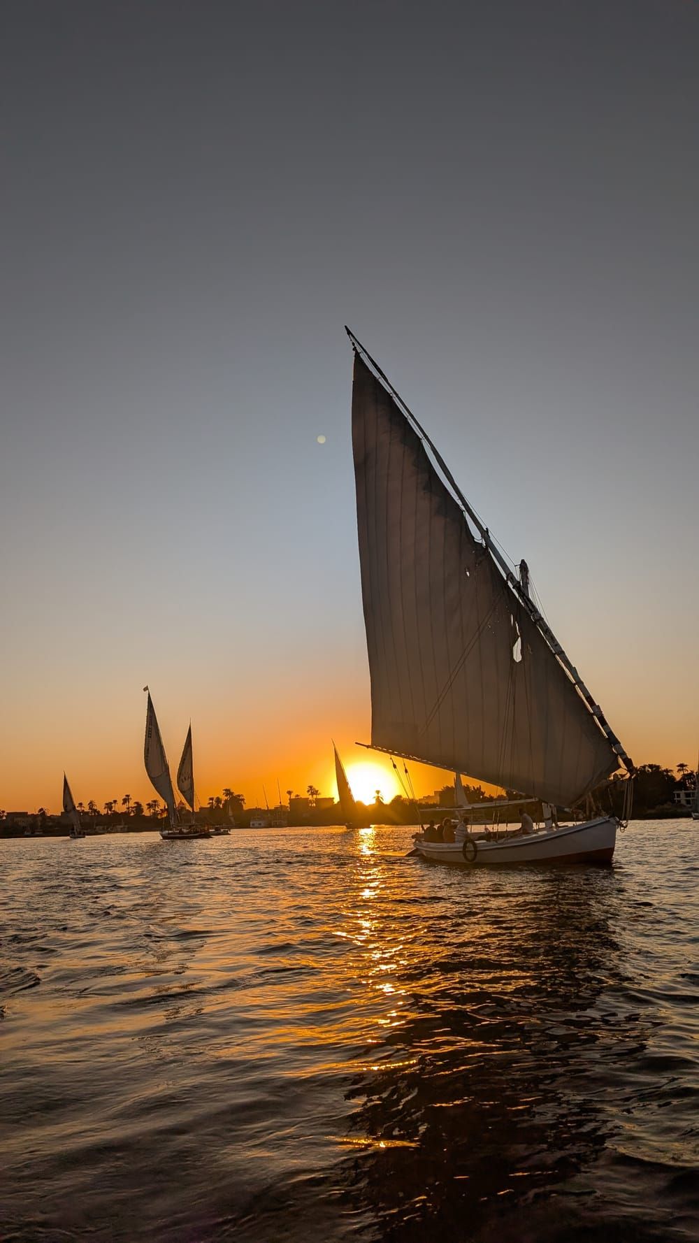 Feluccas sailing on the Nile in Luxor at sunset, silhouetted against the setting sun.