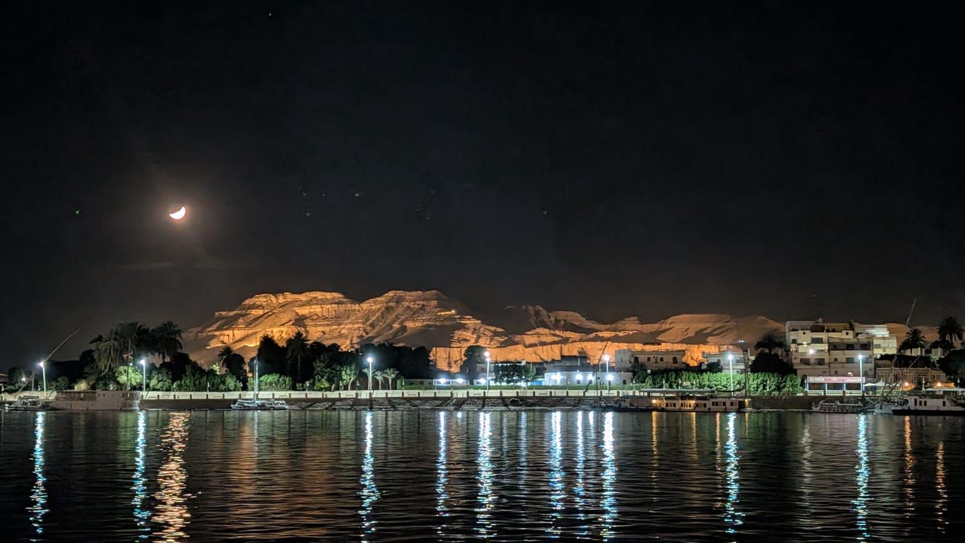 Luxor's West Bank and the Theban Mountain illuminated at night, reflected across the Nile.