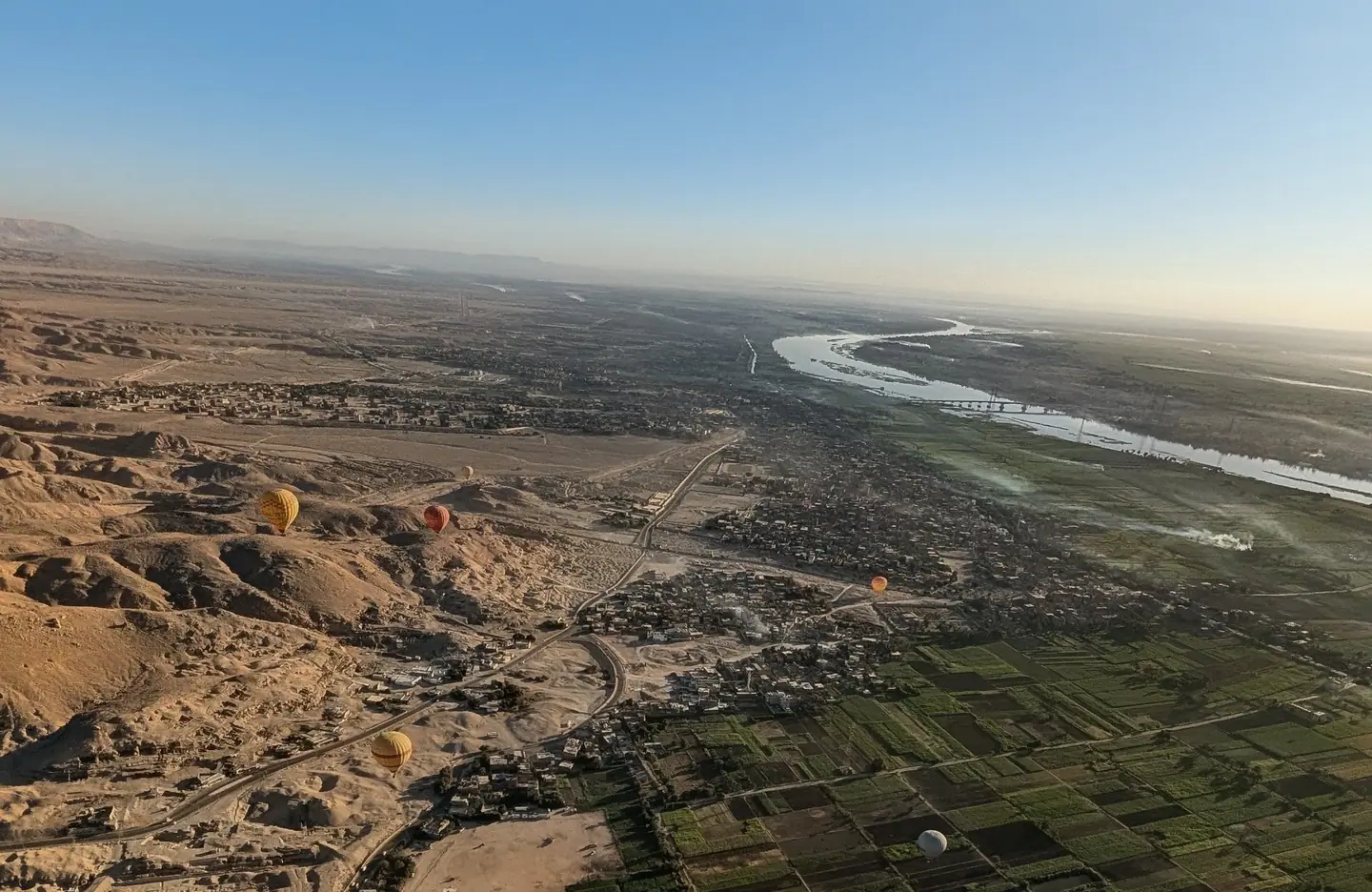 Aerial view across Luxor, showing cultivated land, settlement, desert and hot-air balloons.